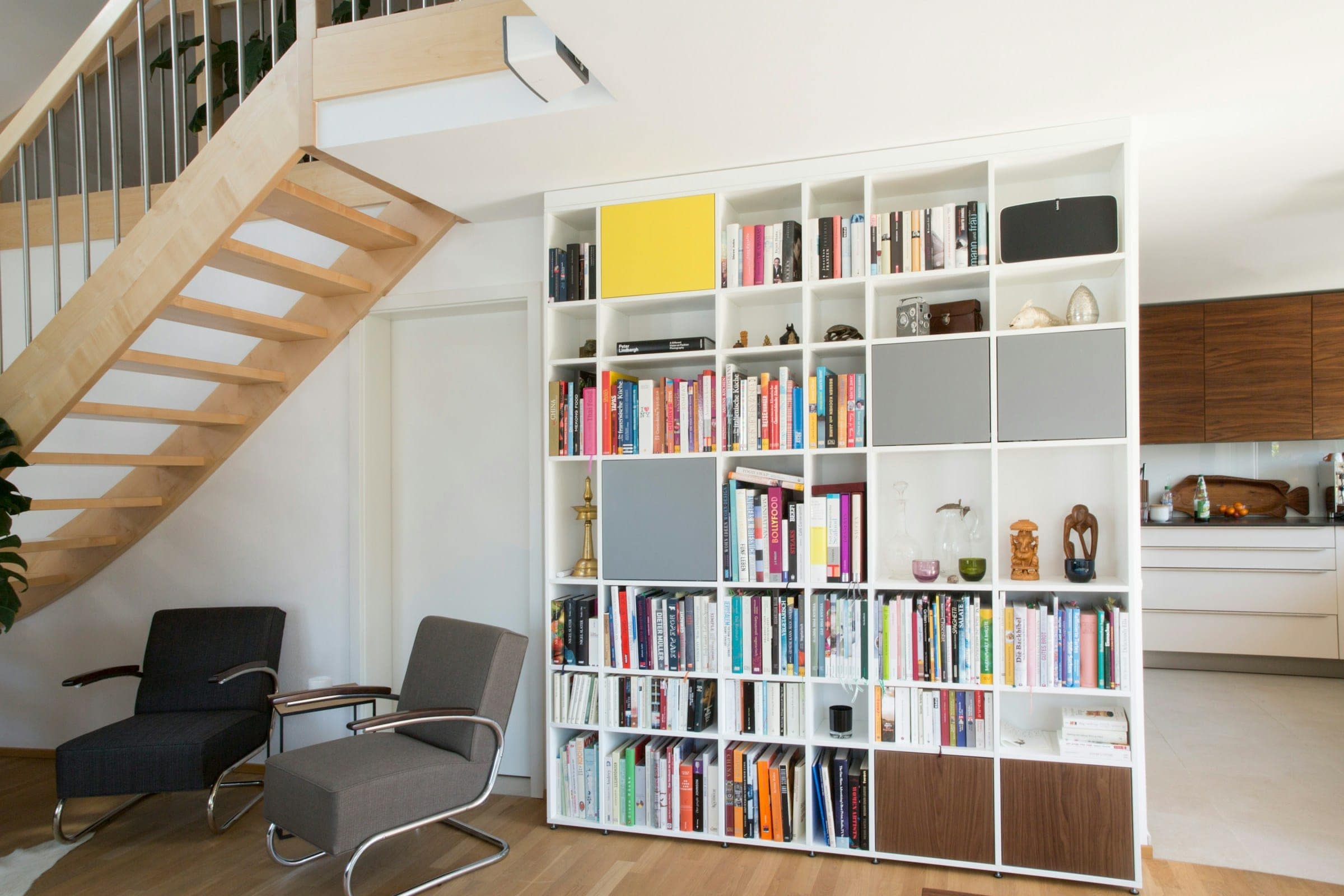Raumhohe weiße Regalwand mit Büchern neben einer Holztreppe